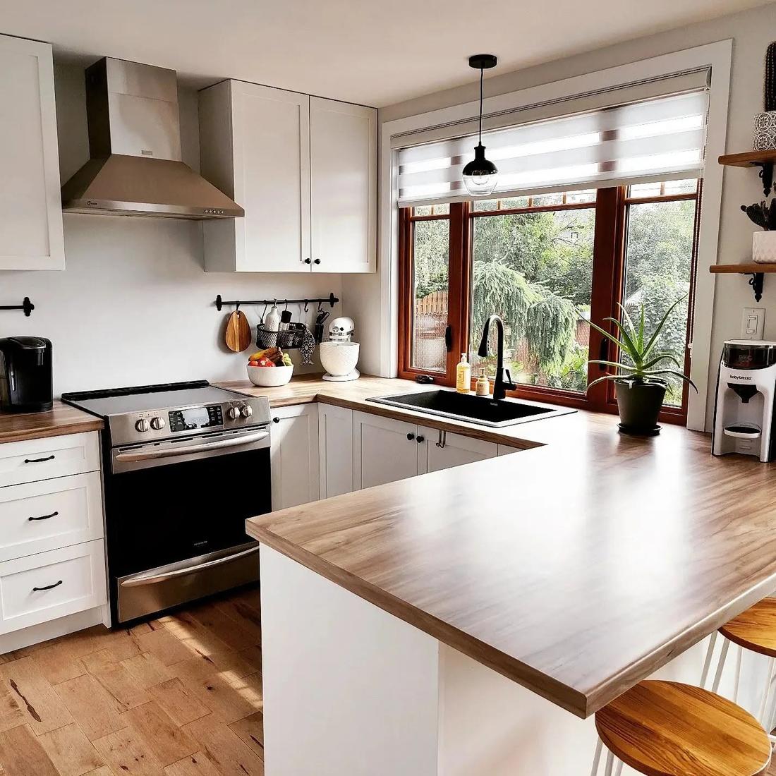 La cuisine après rénovation : armoires blanches, comptoirs de bois massif, grande fenêtre sur la cour et plancher de bois franc
